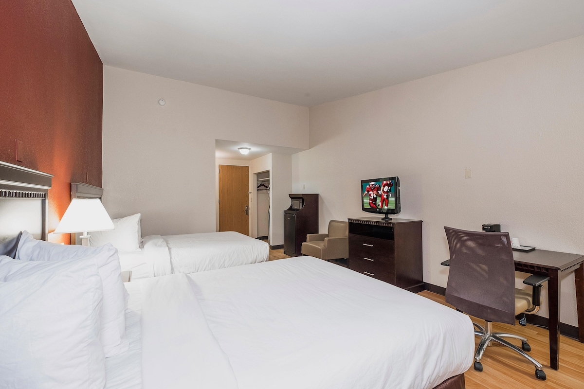 Habitación de hotel con dos camas, un escritorio, una silla, un televisor y un armario.