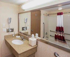 Bany amb un lavabo amb taulell de granit, mirall, assecador d'eixugat, dutxa amb barana de seguretat i suport per a tovalloles.