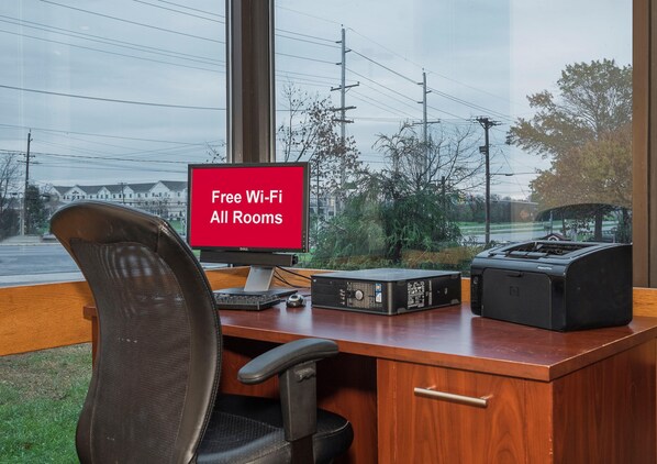 A hotel room with a desk, a computer, a printer, and a sign indicating free Wi-Fi availability. - Red Roof Inn & Suites Mt Holly - Mcguire AFB (Mount Holly)