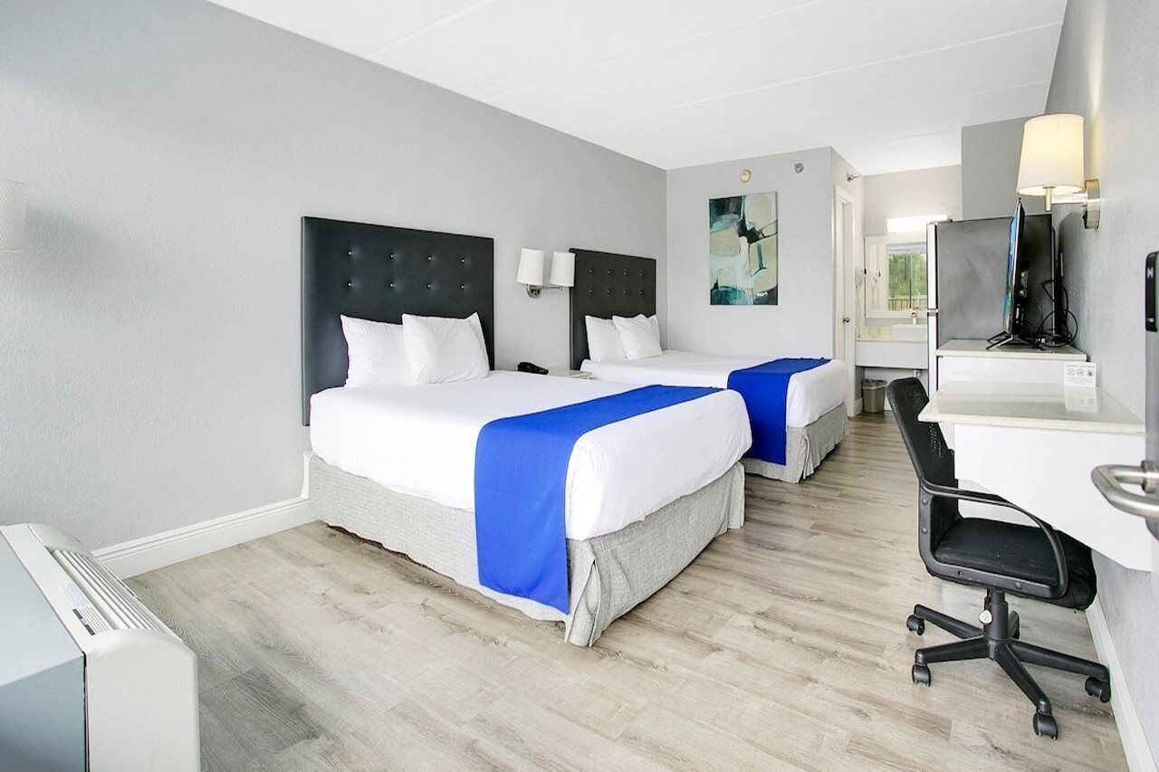 Hotelkamer met twee bedden, een bureau, een stoel, een televisie en een badkamer zichtbaar door een geopende deur.