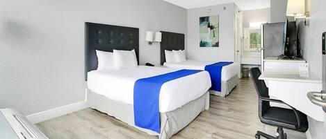 Habitación de hotel con dos camas, un escritorio, una silla, un televisor y un baño visible a través de una puerta abierta.