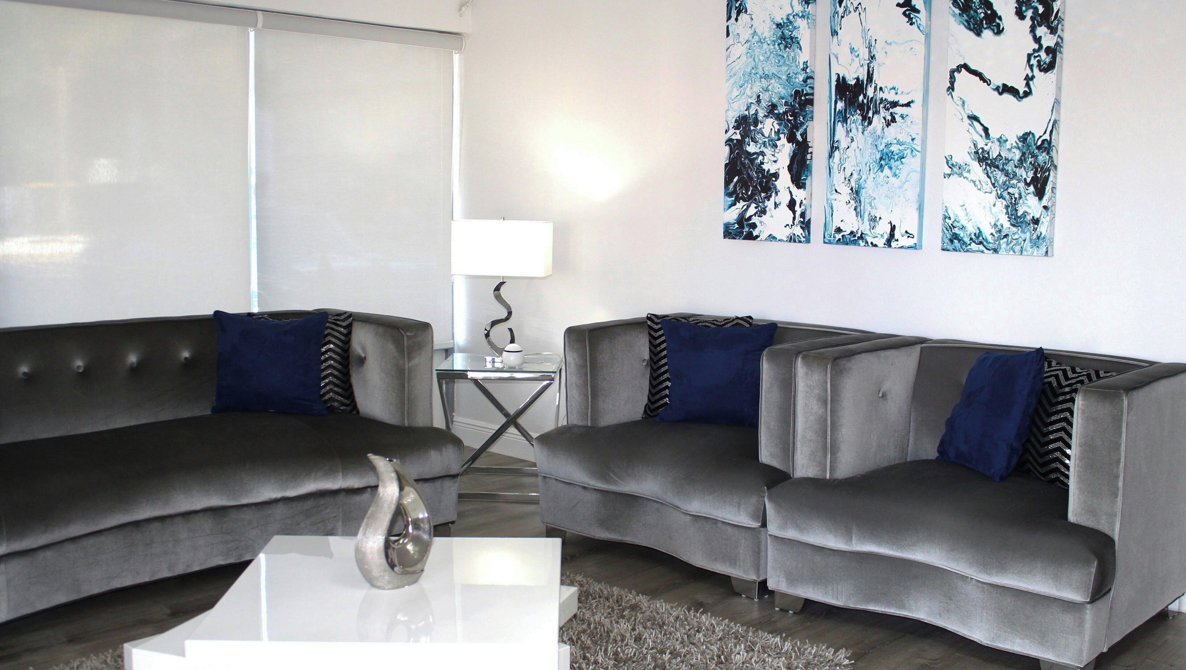 A modern living room with two grey sofas, a glass coffee table, and abstract art on the wall.
