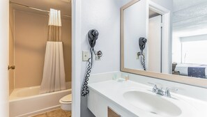 A bathroom with a bathtub, toilet, and a sink with a mirror. There is a hairdryer mounted on the wall. - Home 1 Suites Extended Stay - Kissimmee (Kissimmee)