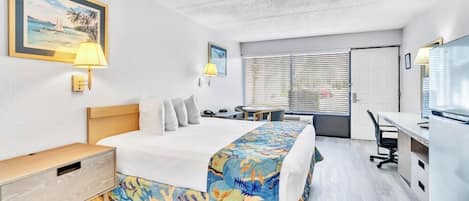 Une chambre d’hôtel comprenant un lit, une table de chevet, une lampe, un bureau, une chaise et une fenêtre avec des stores.