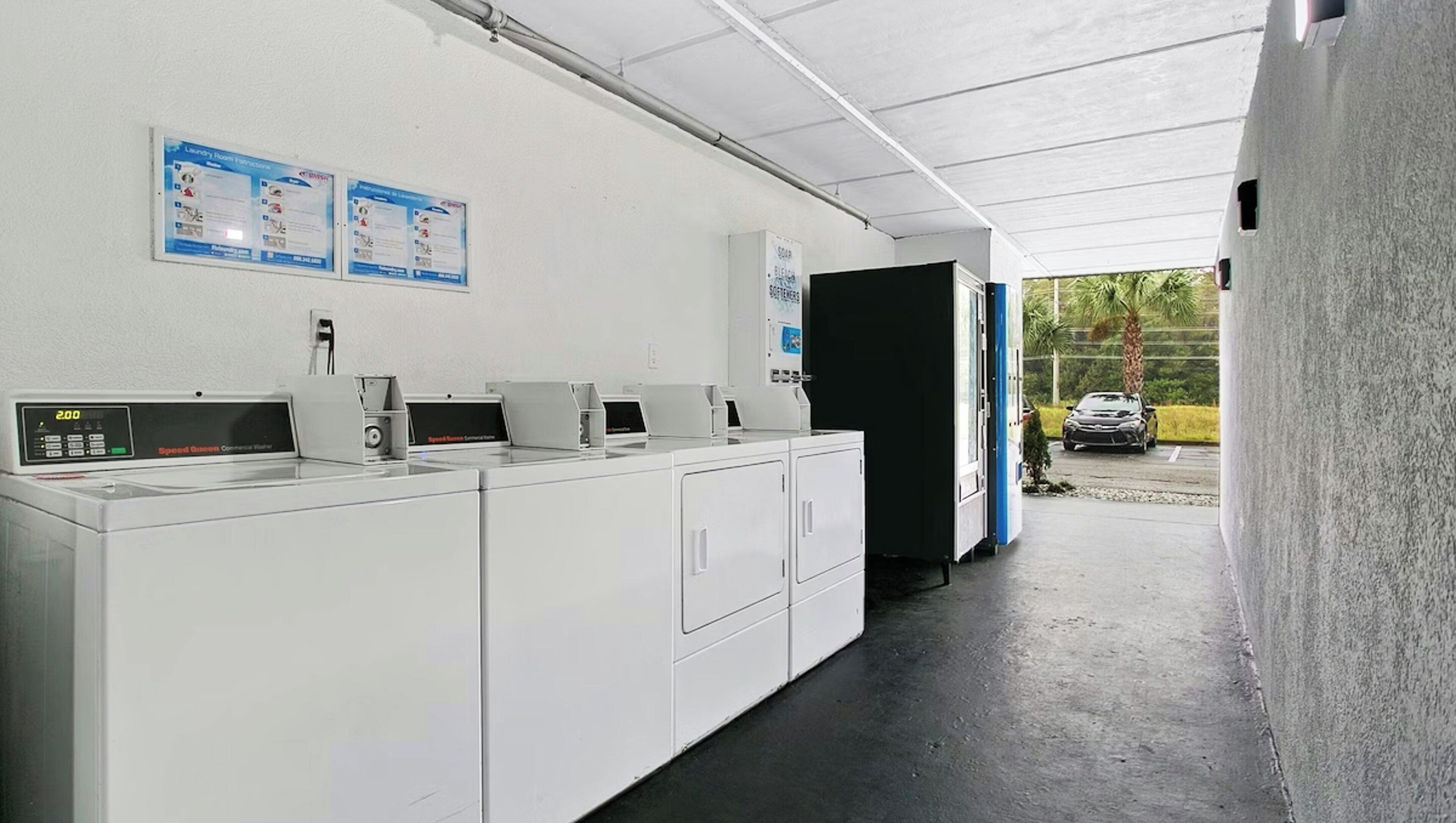 Un cuarto de lavandería con varias lavadoras, una pantalla digital y carteles informativos en la pared.