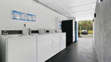 Un cuarto de lavandería con varias lavadoras, una pantalla digital y carteles informativos en la pared.