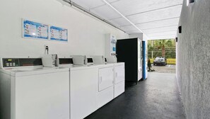 A laundry facility with multiple washing machines, a digital display, and instructional posters on the wall. - Home 1 Suites Extended Stay - Kissimmee (Kissimmee)