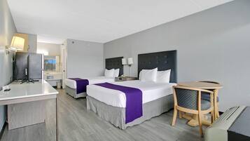 A hotel room with two beds, a desk, a chair, and a small table.