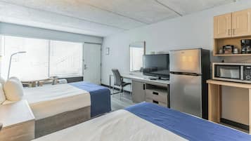 A hotel room with two beds, a desk with a television, a refrigerator, and a microwave.