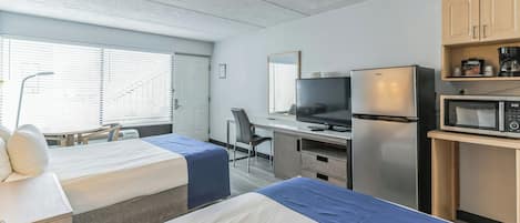 A hotel room with two beds, a desk with a television, a refrigerator, and a microwave.