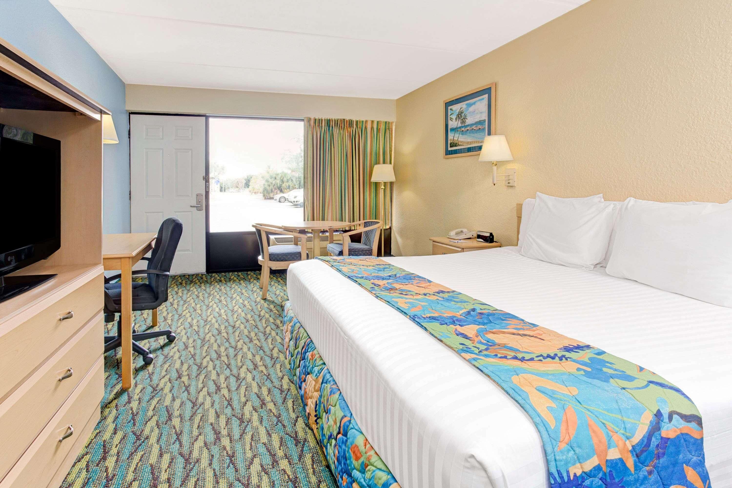 A hotel room with a bed, a desk, a chair, a television, and a door.