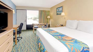 A hotel room with a bed, a desk, a chair, a television, and a door.