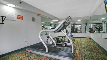 A fitness center with a treadmill, mirrors, and a carpeted floor.