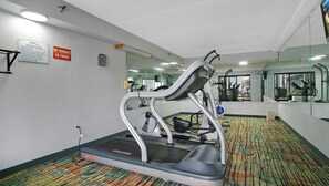 Un gimnasio con cinta de correr, espejos y piso alfombrado.