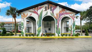 A building with a white facade and colorful tropical leaf murals, featuring three arches and a central entrance.