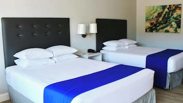 Habitación de hotel con dos camas, cada una con ropa de cama blanca y un detalle en azul. Hay dos mesitas de noche con lámparas y un cuadro en la pared.