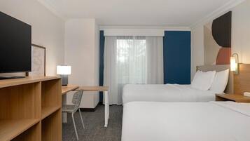 A hotel room with two beds, a desk, a chair, a TV, and a window with curtains.