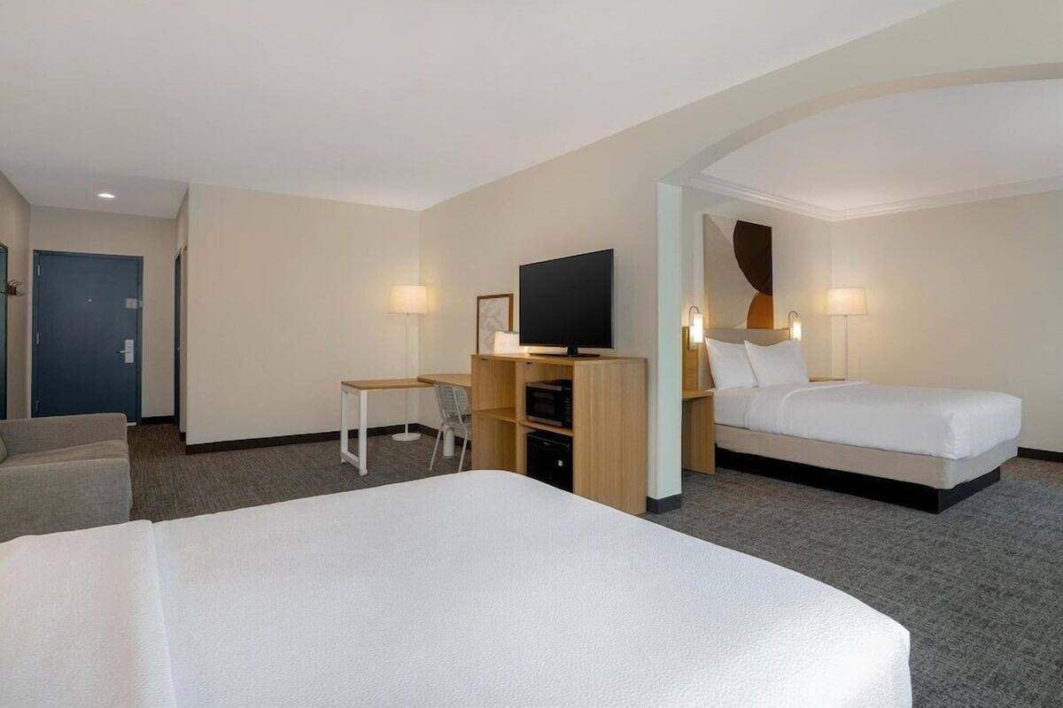 A hotel room with a large bed, a smaller bed, a desk with a chair, a television, and a door.