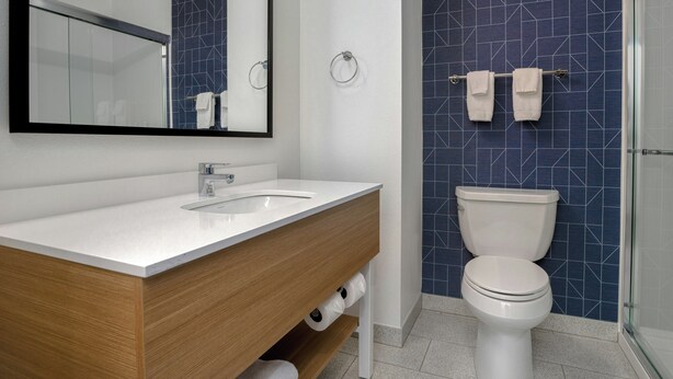 Un baño moderno con lavamanos blanco, tocador de madera, inodoro y cabina de ducha de vidrio.