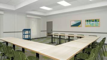 Un salón de conferencias con una larga mesa, sillas verdes y dos cuadros abstractos en la pared.
