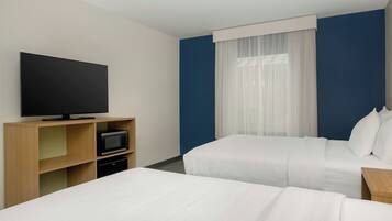 Une chambre d’hôtel avec deux lits, un téléviseur à écran plat, un four à micro-ondes et une fenêtre avec des rideaux légers.