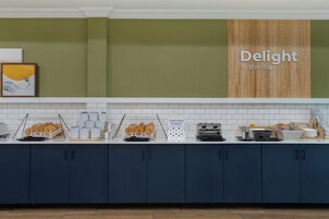 Un bufé de desayuno con diversas opciones de comida y un letrero que dice 'Delight in the day'.