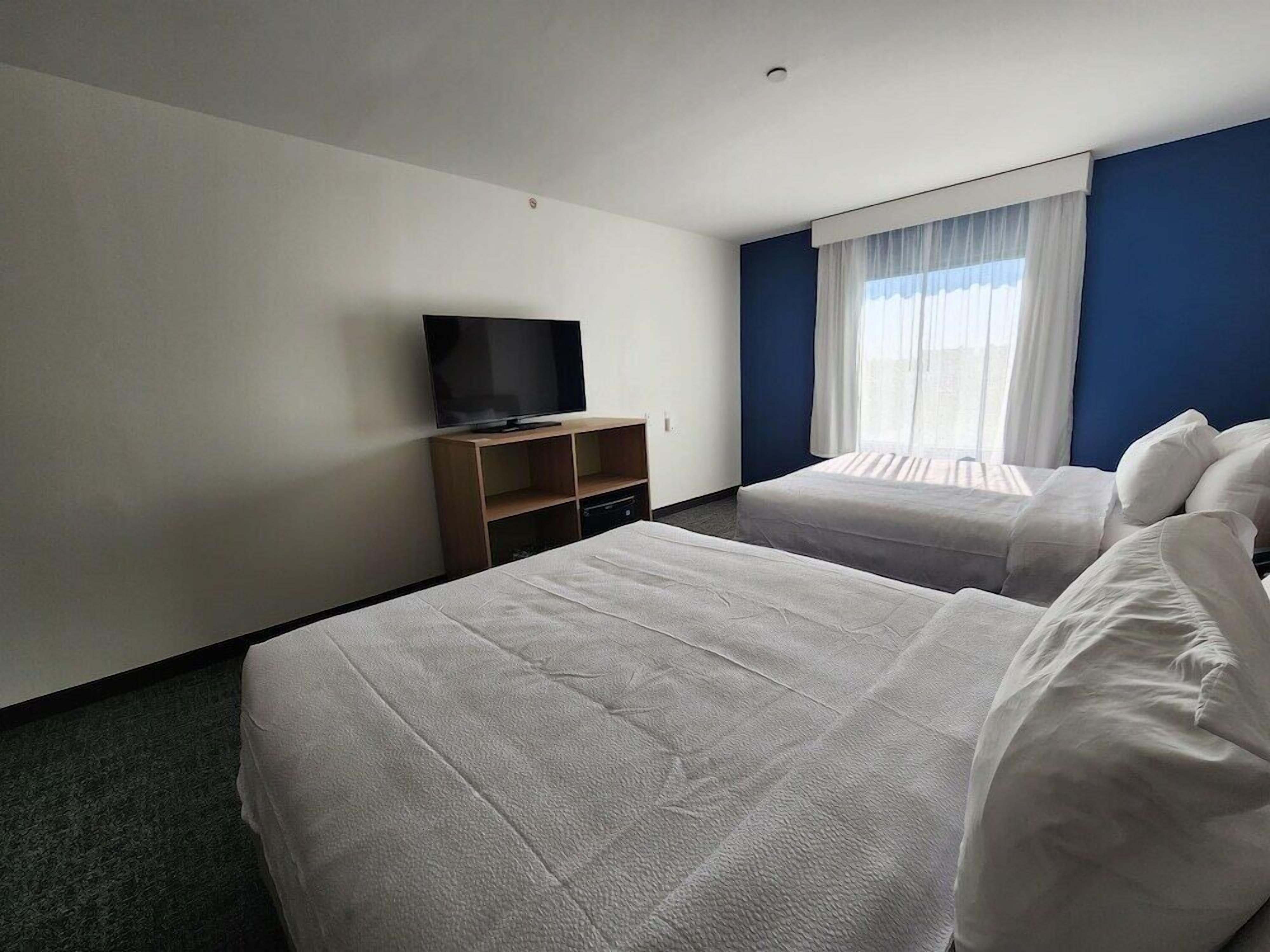 Una habitación de hotel con dos camas, un televisor sobre un mueble de madera y una ventana con cortinas.