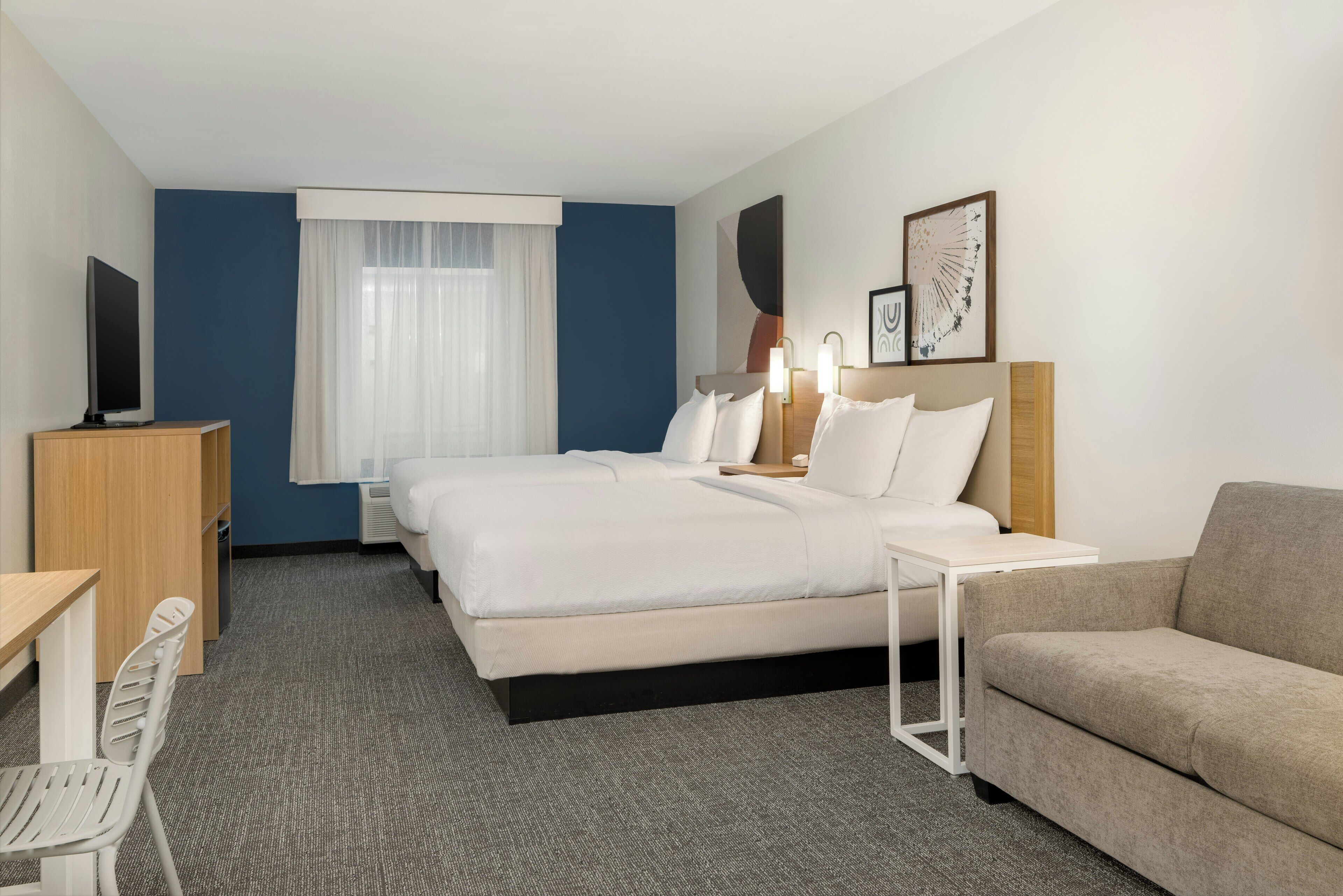 A hotel room with a bed, a desk, a chair, a sofa, and a TV.