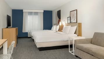 A hotel room with a bed, a desk, a chair, a sofa, and a TV.