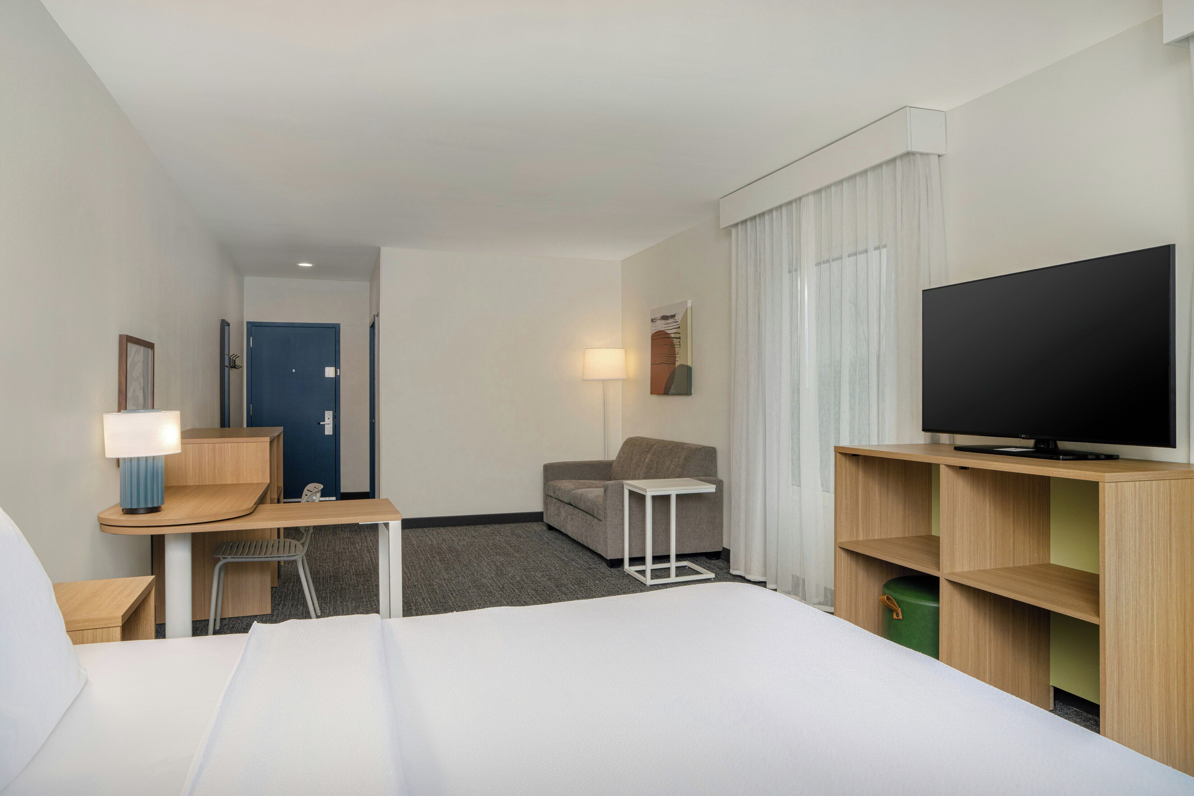Habitación de hotel con cama, escritorio con lámpara, televisión, sofá y una pequeña mesa.