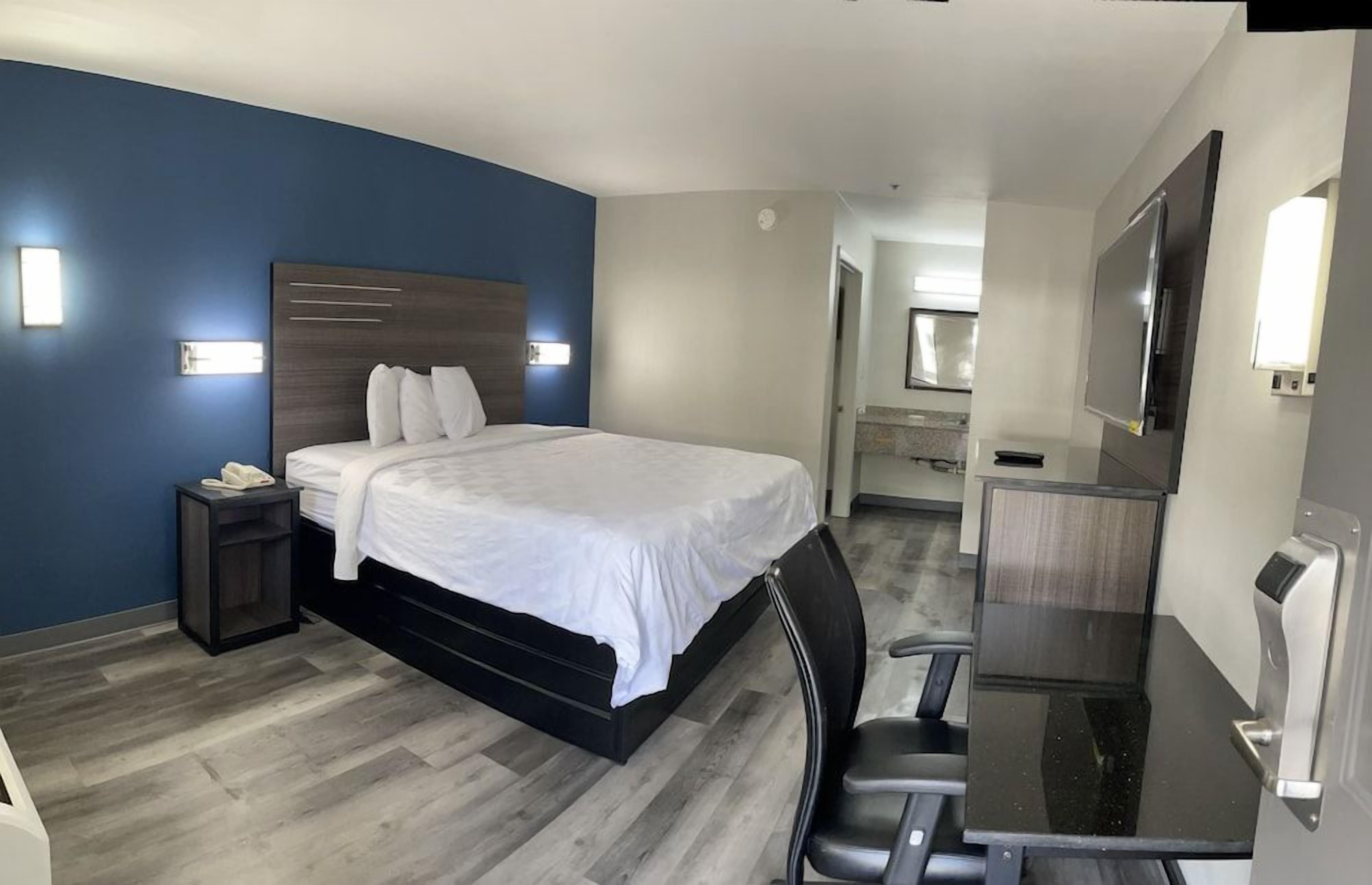 A hotel room with a bed, a desk, a chair, a phone, and a TV.