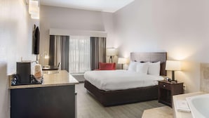 A hotel room with a bed, bedside tables, a desk with a chair, a large window with curtains, and a bathroom with a bathtub. - Comfort Inn & Suites Fairburn - Atlanta Southwest (Fairburn)