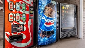 Two beverage vending machines, one with Coca-Cola and the other with Pepsi branding, next to a glass door. - Hometowne Studios Atlanta - Chamblee (Chamblee)