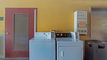 A laundry facility with washers and dryers, a detergent dispenser, and a sign indicating soap, bleach, and softeners are available.