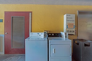 A laundry facility with washers and dryers, a detergent dispenser, and a sign indicating soap, bleach, and softeners are available. - Suburban Studios Hinesville - Fort Stewart Area (Hinesville)