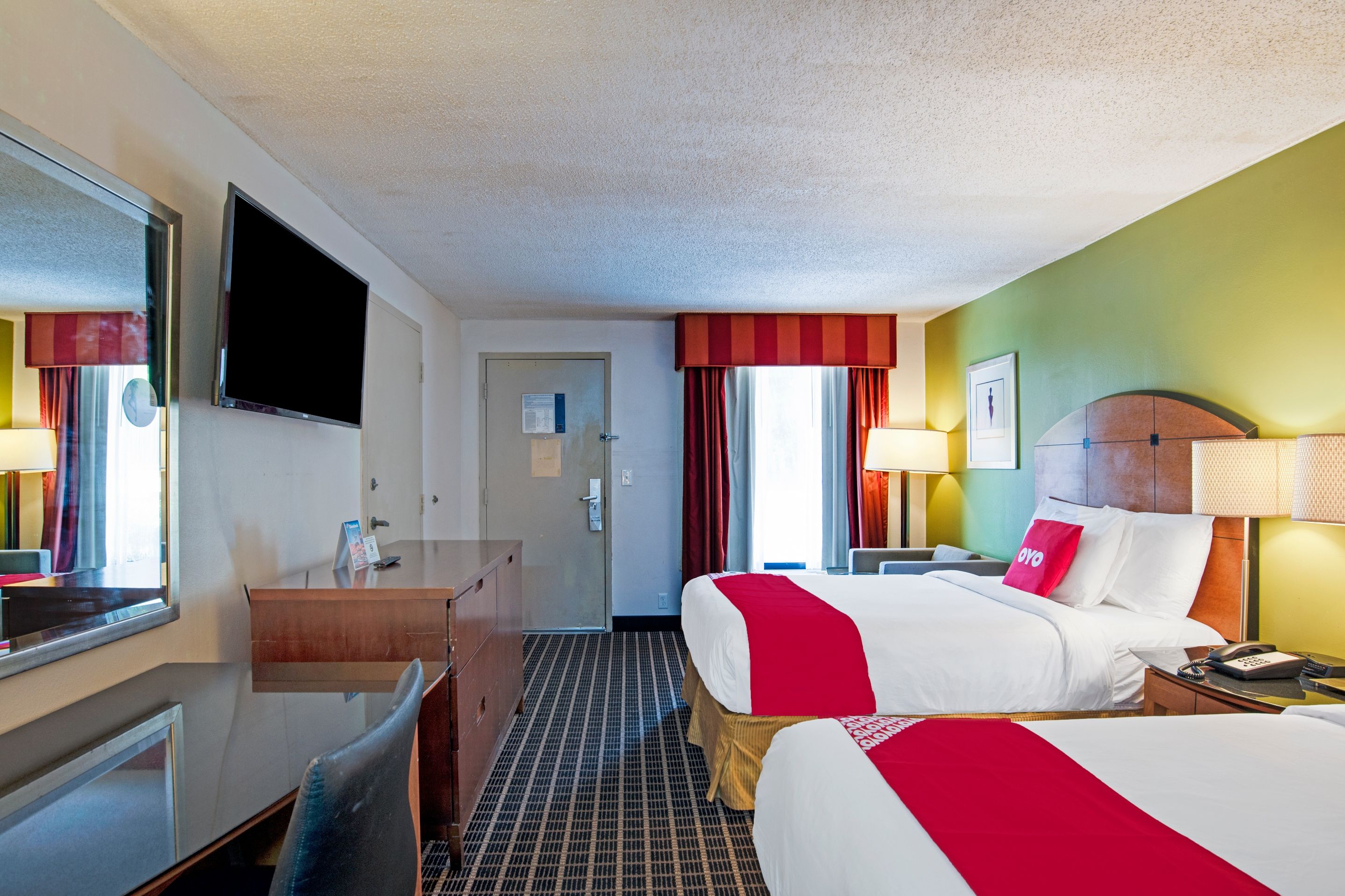 A hotel room with two beds, a desk, a TV, and a door.
