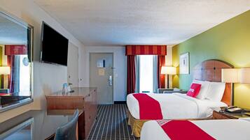 A hotel room with two beds, a desk, a TV, and a door.