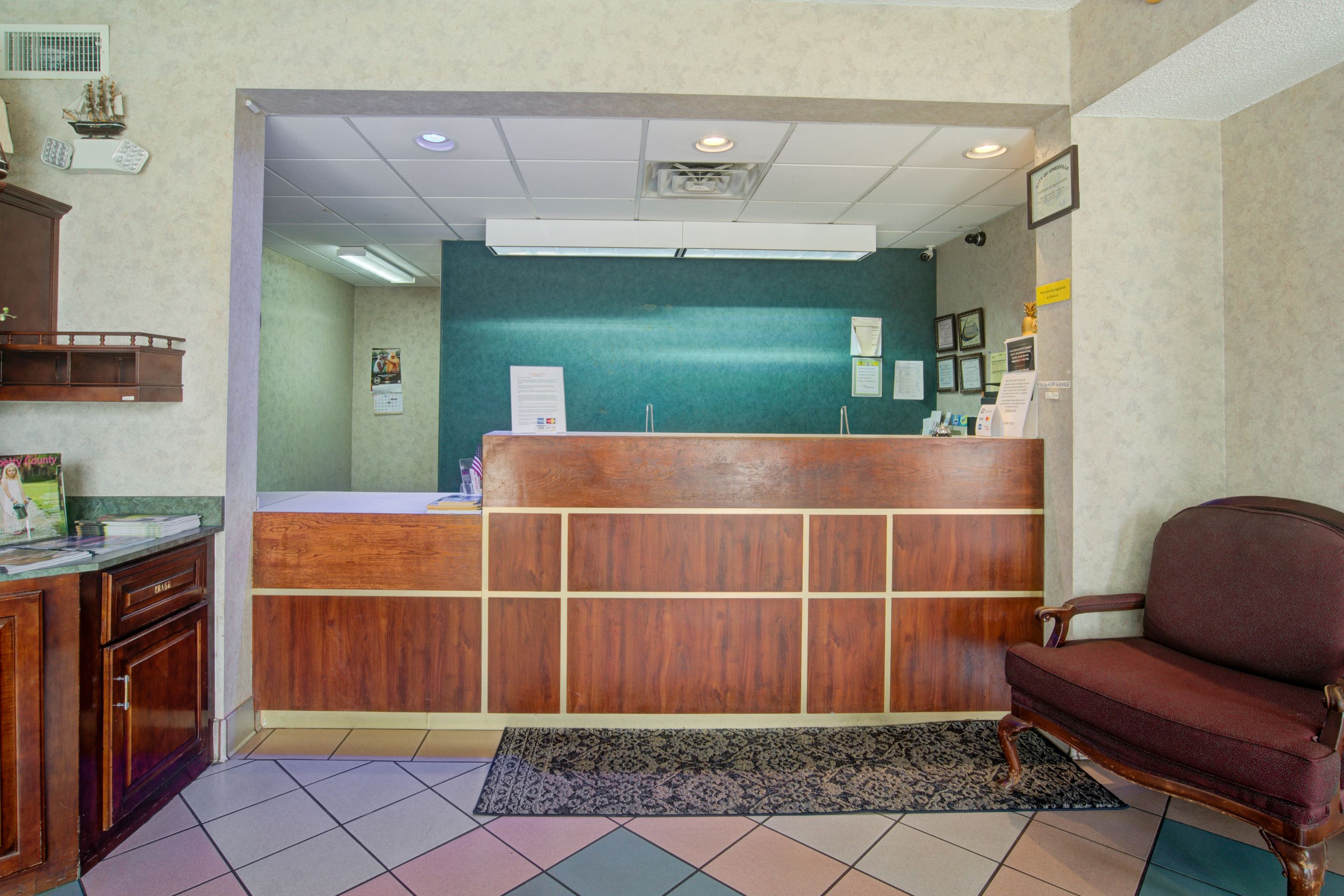 A reception area with a wooden reception desk, a dark patterned rug, and a brown chair.