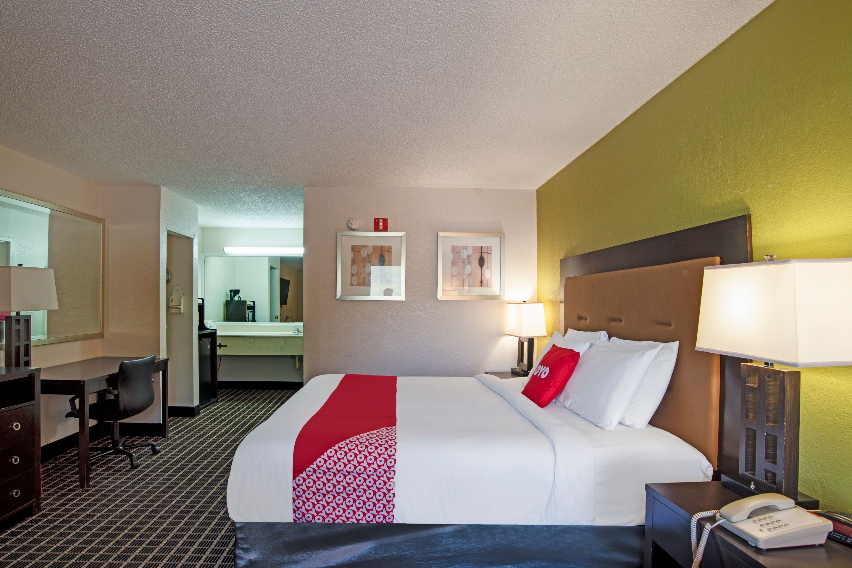 Ein Hotelzimmer mit Bett, Nachttisch, Lampe, Telefon, Schreibtisch, Stuhl und Spiegel.