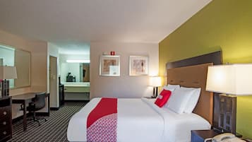 Ein Hotelzimmer mit Bett, Nachttisch, Lampe, Telefon, Schreibtisch, Stuhl und Spiegel.