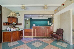 A reception area with a wooden desk, a reception counter, a decorative ship model, and a vintage chair. - Suburban Studios Hinesville - Fort Stewart Area (Hinesville)