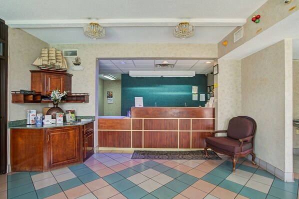 A reception area with a wooden desk, a reception counter, a decorative ship model, and a vintage chair. - Suburban Studios Hinesville - Fort Stewart Area (Hinesville)