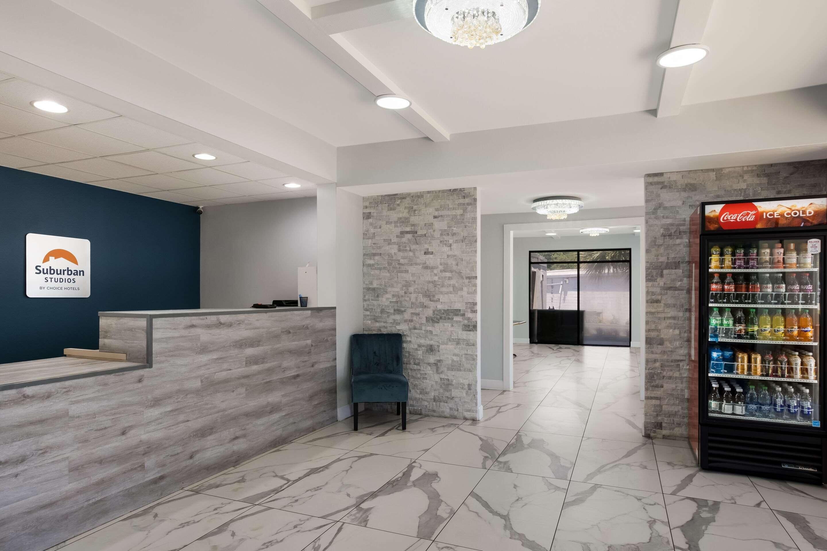 A reception area with a blue wall, a reception desk, a chair, a Coca-Cola fridge, and a stone wall.