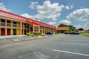 Un motel con techo rojo, paredes amarillas y estacionamiento.