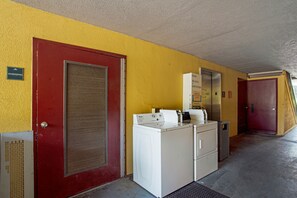 A laundry area with a red door, a white washing machine, and a small cabinet. - Suburban Studios Hinesville - Fort Stewart Area (Hinesville)