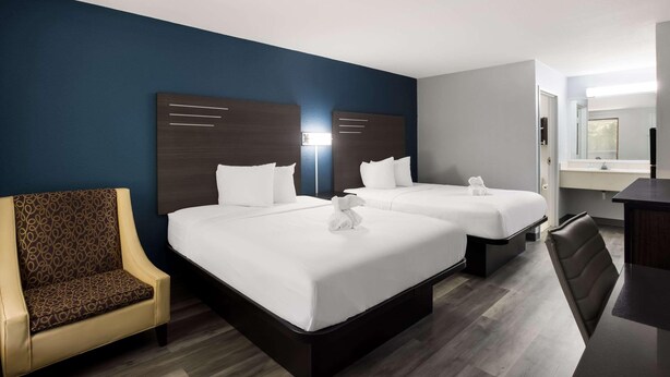 Quarto de hotel com duas camas, uma cadeira, uma escrivaninha e um espelho.