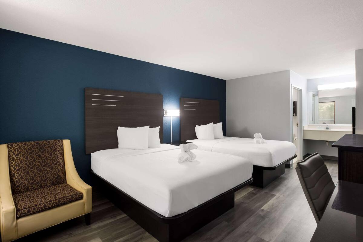 Una habitación de hotel con dos camas, una silla, un escritorio y un espejo.