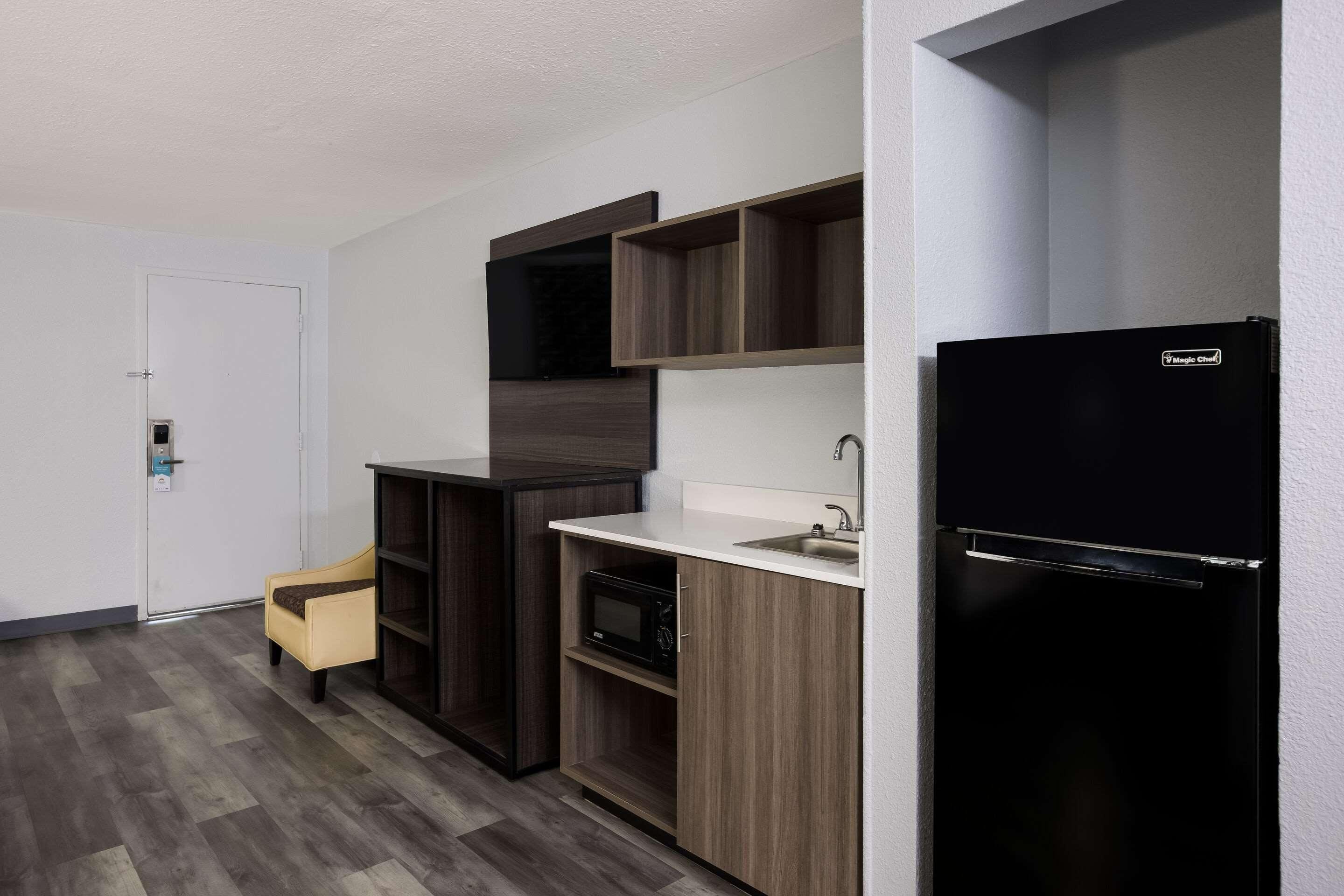 A compact kitchen with a microwave, a refrigerator, and wooden cabinets.