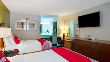 A hotel room with two beds, a desk, a chair, a TV, and a bathroom visible through an open door.