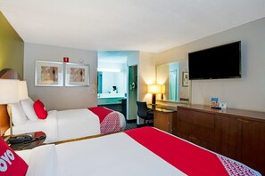 Een hotelkamer met twee bedden, een bureau, een stoel, een televisie en een badkamer die door een open deur zichtbaar is.